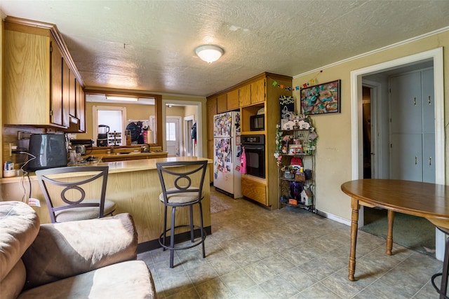 kitchen featuring black appliances, a kitchen breakfast bar, kitchen peninsula, crown molding, and a textured ceiling