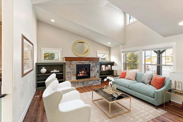 living room featuring wood-type flooring, a stone fireplace, a healthy amount of sunlight, and high vaulted ceiling