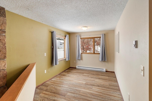 corridor featuring a textured ceiling, baseboard heating, and light hardwood / wood-style floors