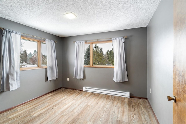 spare room featuring light hardwood / wood-style floors, a textured ceiling, and a baseboard heating unit