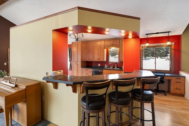 kitchen with sink, a breakfast bar, hanging light fixtures, a textured ceiling, and stainless steel dishwasher