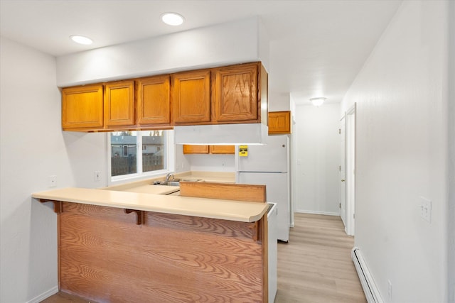 kitchen featuring a breakfast bar, sink, kitchen peninsula, white fridge, and a baseboard heating unit