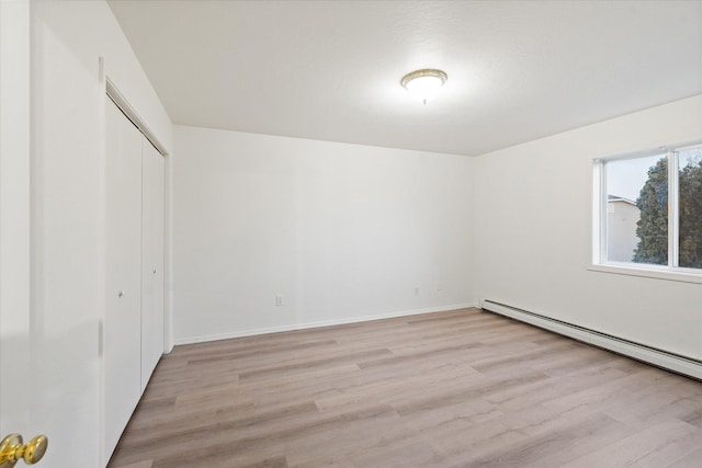 unfurnished bedroom featuring a baseboard radiator, light wood-type flooring, and a closet