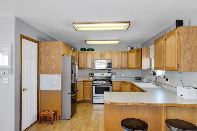 kitchen featuring appliances with stainless steel finishes, sink, a kitchen breakfast bar, kitchen peninsula, and light wood-type flooring