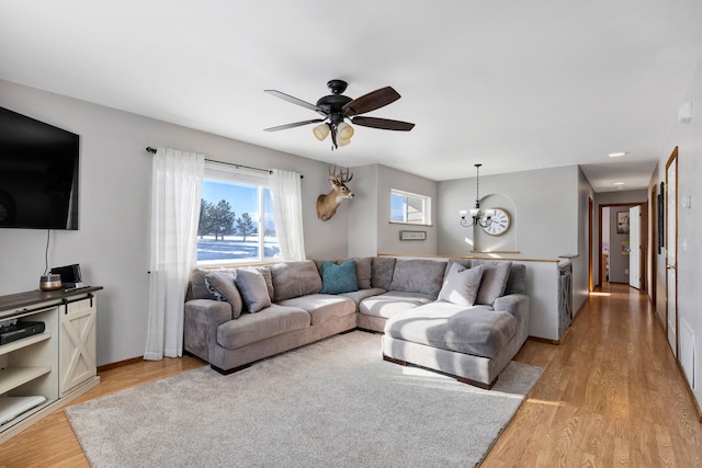 living room with ceiling fan with notable chandelier and light hardwood / wood-style flooring