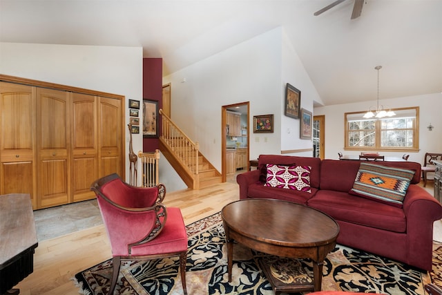 living room with ceiling fan with notable chandelier, high vaulted ceiling, and light hardwood / wood-style flooring