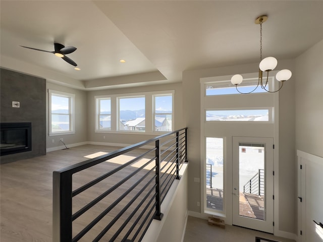 foyer featuring ceiling fan with notable chandelier, hardwood / wood-style floors, a large fireplace, a raised ceiling, and a mountain view