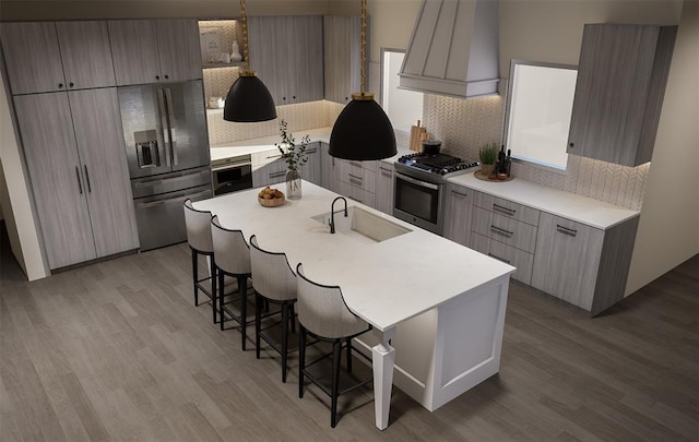 kitchen with sink, a kitchen breakfast bar, stainless steel appliances, custom range hood, and an island with sink