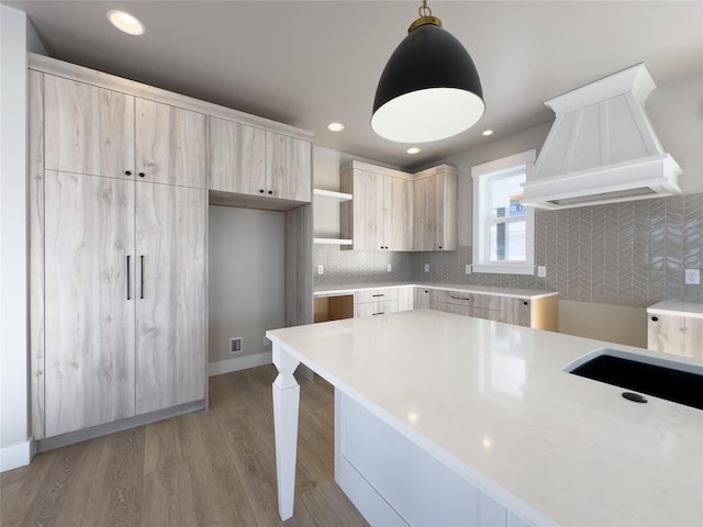 kitchen featuring light brown cabinetry, decorative light fixtures, custom range hood, light hardwood / wood-style floors, and decorative backsplash