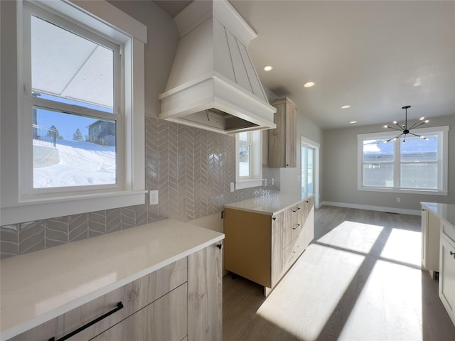 kitchen featuring premium range hood, an inviting chandelier, light wood-type flooring, and decorative backsplash