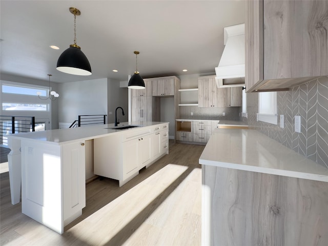 kitchen with sink, light hardwood / wood-style flooring, hanging light fixtures, a center island, and custom exhaust hood