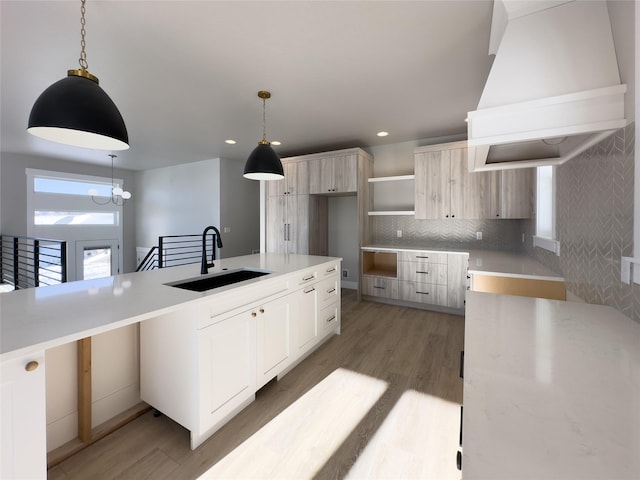 kitchen featuring sink, premium range hood, light brown cabinetry, decorative light fixtures, and light wood-type flooring