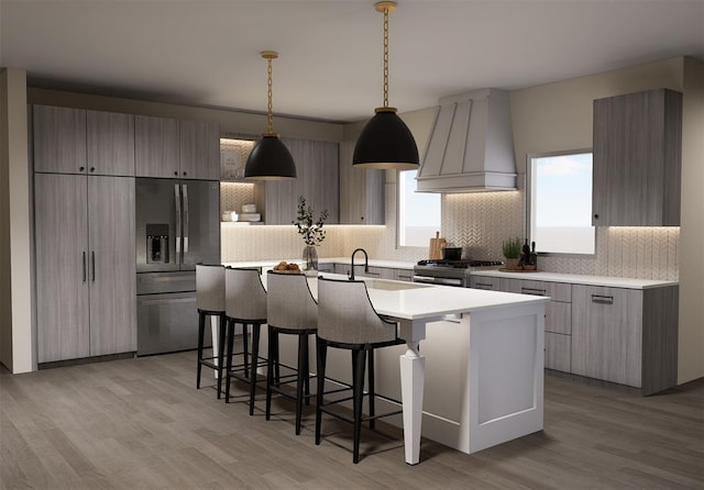 kitchen featuring custom exhaust hood, decorative light fixtures, a center island with sink, appliances with stainless steel finishes, and decorative backsplash