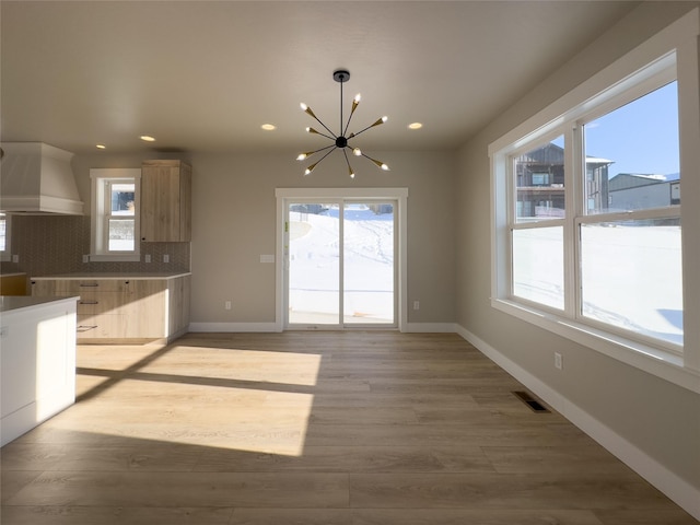 kitchen featuring light wood-type flooring, wall chimney range hood, backsplash, and light brown cabinets