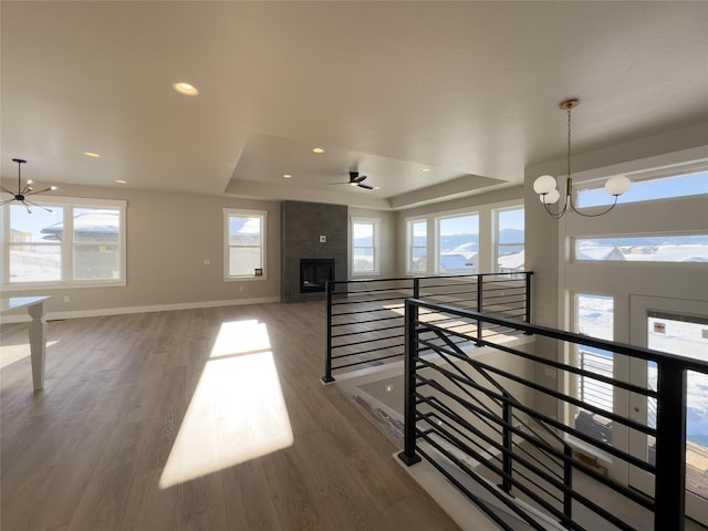 unfurnished living room featuring a wealth of natural light, wood-type flooring, a raised ceiling, and ceiling fan with notable chandelier