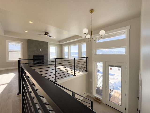 corridor featuring a healthy amount of sunlight, light wood-type flooring, and a tray ceiling