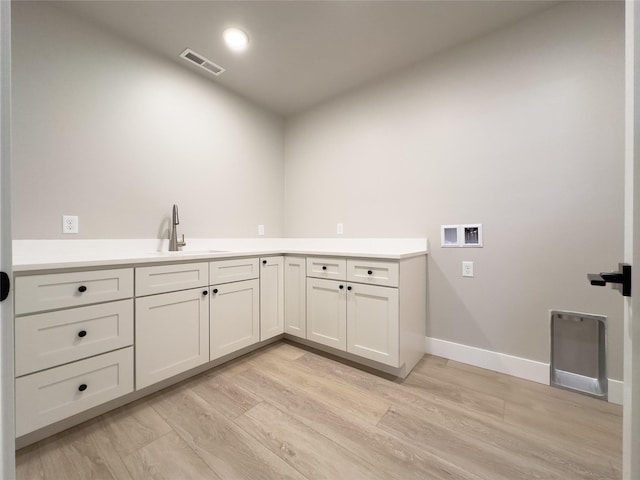 washroom with washer hookup, sink, light hardwood / wood-style flooring, and cabinets