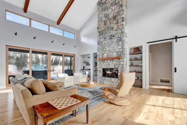 living room featuring built in features, vaulted ceiling with beams, a fireplace, a barn door, and light wood-type flooring