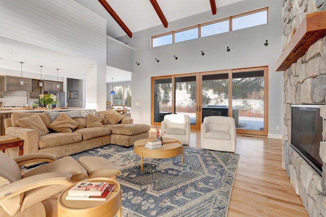 living room with beam ceiling, a stone fireplace, high vaulted ceiling, and light wood-type flooring