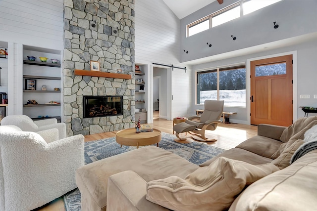 living room featuring a barn door, a wealth of natural light, a stone fireplace, and light hardwood / wood-style floors