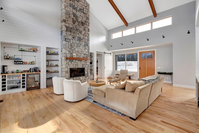 living room with a stone fireplace, light hardwood / wood-style floors, a barn door, bar area, and beam ceiling