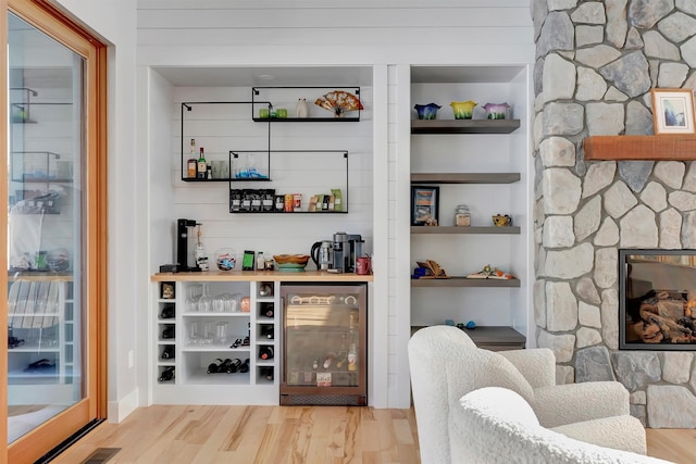 bar featuring built in features, wine cooler, a fireplace, and light hardwood / wood-style flooring