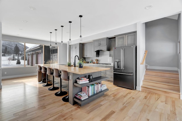 kitchen featuring pendant lighting, appliances with stainless steel finishes, gray cabinets, and an island with sink