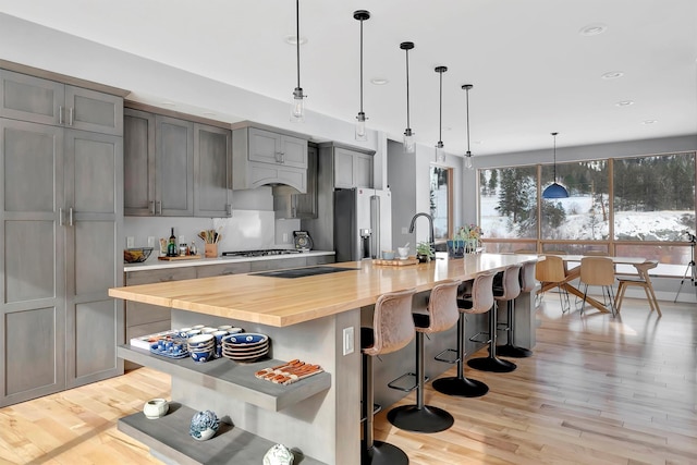 kitchen featuring gray cabinets, appliances with stainless steel finishes, a breakfast bar, hanging light fixtures, and a large island with sink