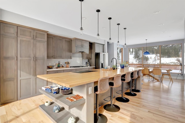 kitchen with a large island, wooden counters, appliances with stainless steel finishes, light hardwood / wood-style floors, and decorative light fixtures