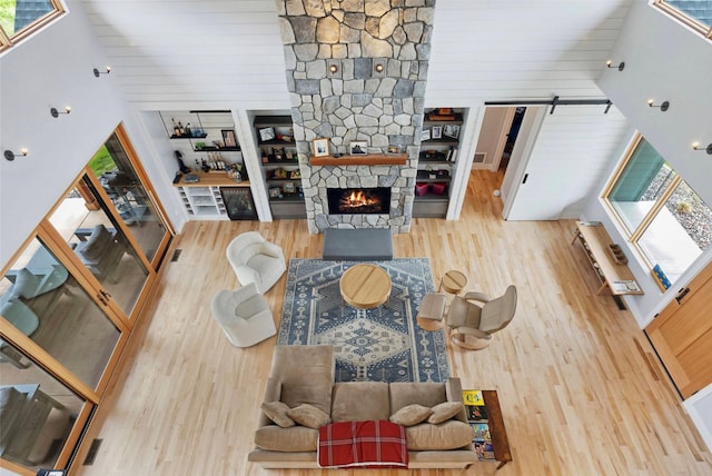 living room featuring a high ceiling, a stone fireplace, a healthy amount of sunlight, and hardwood / wood-style floors