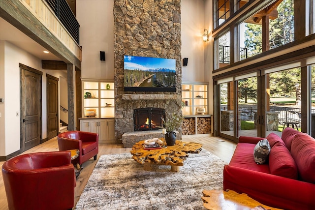 living room with a stone fireplace, light hardwood / wood-style flooring, and a towering ceiling