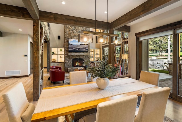 dining area with beam ceiling, hardwood / wood-style flooring, and a fireplace