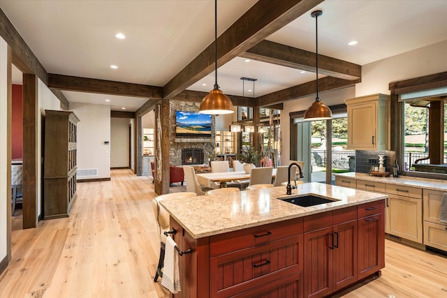 113 Levi Ct, Bigfork, MT 59911 - kitchen featuring beamed ceiling, light wood finished floors, open floor plan, a stone fireplace, and a center island with sink