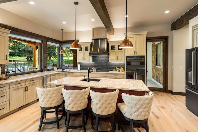 kitchen featuring hanging light fixtures, premium range hood, and a center island with sink