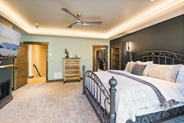 bedroom featuring a tray ceiling, a walk in closet, ceiling fan, and carpet