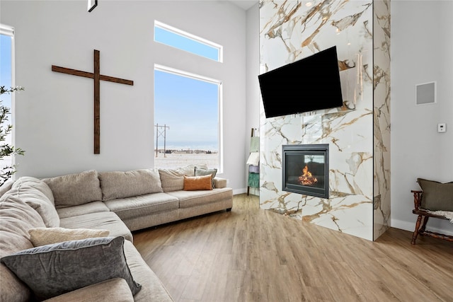 living room with hardwood / wood-style flooring, a healthy amount of sunlight, a fireplace, and a towering ceiling