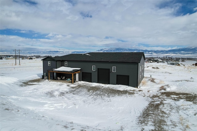 snow covered structure with a garage and a mountain view