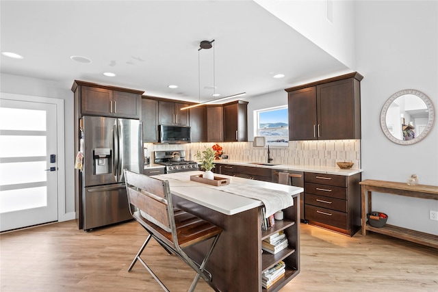 kitchen featuring sink, appliances with stainless steel finishes, hanging light fixtures, light hardwood / wood-style floors, and a kitchen island