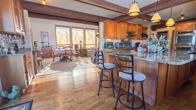 kitchen with decorative light fixtures, light hardwood / wood-style flooring, appliances with stainless steel finishes, dark stone counters, and beam ceiling