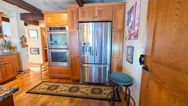6809 N Montana Ave, Helena, MT 59602 - kitchen featuring appliances with stainless steel finishes, light wood-style floors, beamed ceiling, light stone counters, and brown cabinets