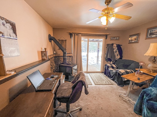 office area with carpet flooring, ceiling fan, and a wood stove