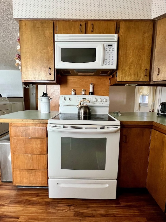 kitchen with dark wood-type flooring, white appliances, and kitchen peninsula