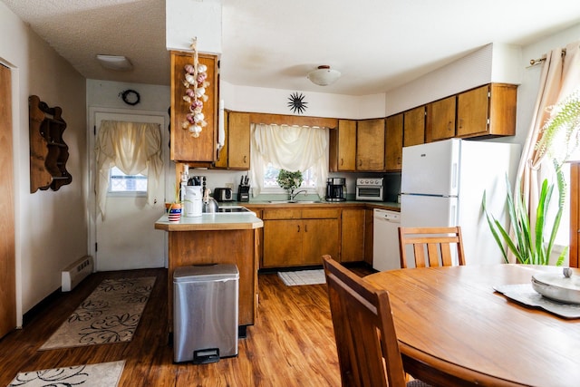 kitchen featuring sink, light wood-type flooring, baseboard heating, plenty of natural light, and white appliances