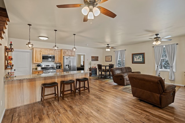 kitchen with a breakfast bar, kitchen peninsula, stainless steel appliances, light brown cabinets, and light wood-type flooring