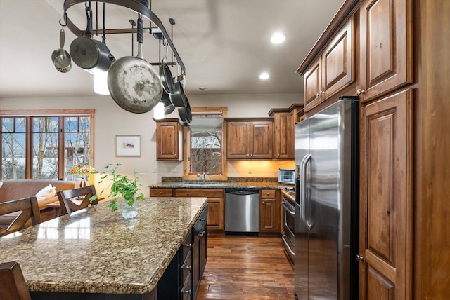 kitchen with stainless steel appliances, dark wood-type flooring, a kitchen island, a sink, and light stone countertops