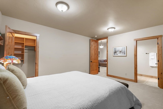 bedroom featuring baseboards, a walk in closet, and light colored carpet