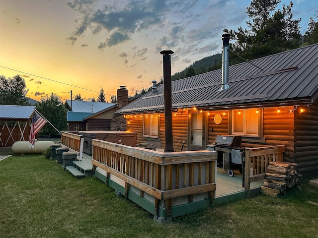 back house at dusk with a hot tub, a deck, and a lawn