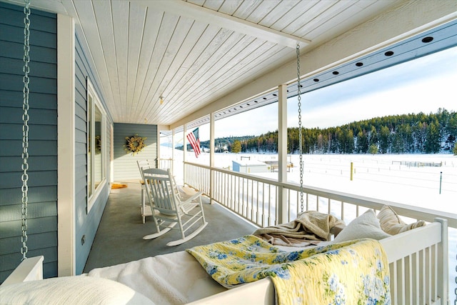snow covered patio with a wooded view and a porch