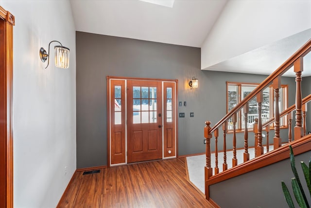 foyer entrance featuring baseboards, vaulted ceiling, wood finished floors, and a healthy amount of sunlight