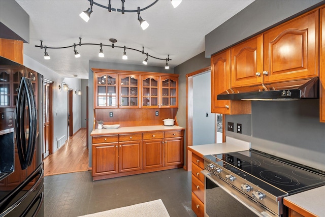 kitchen with under cabinet range hood, electric stove, brown cabinets, and black fridge